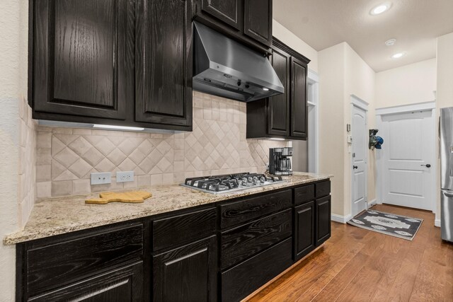 kitchen with backsplash, light stone counters, light wood-type flooring, and appliances with stainless steel finishes