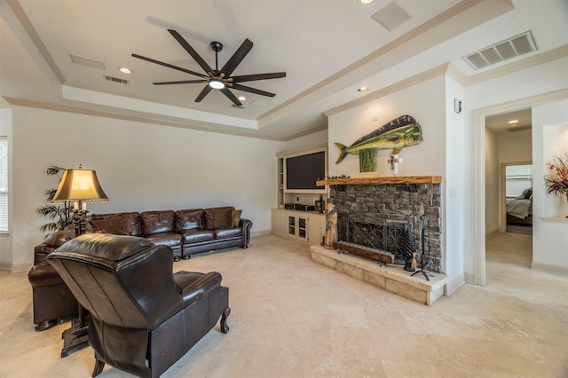 living room featuring ceiling fan, ornamental molding, a stone fireplace, and a raised ceiling