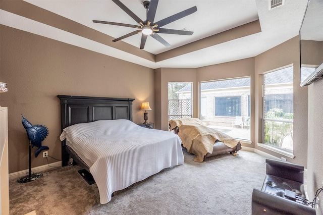 carpeted bedroom with a raised ceiling and ceiling fan