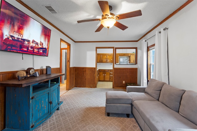 carpeted living room featuring ceiling fan, wood walls, crown molding, and a textured ceiling