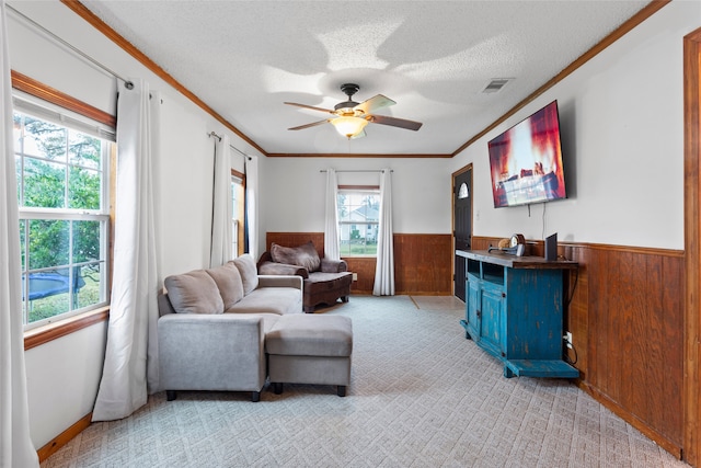 living room featuring wood walls, ceiling fan, ornamental molding, a textured ceiling, and light colored carpet