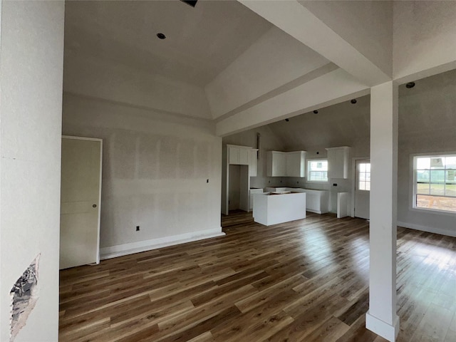 unfurnished living room with a healthy amount of sunlight, dark wood-type flooring, and high vaulted ceiling