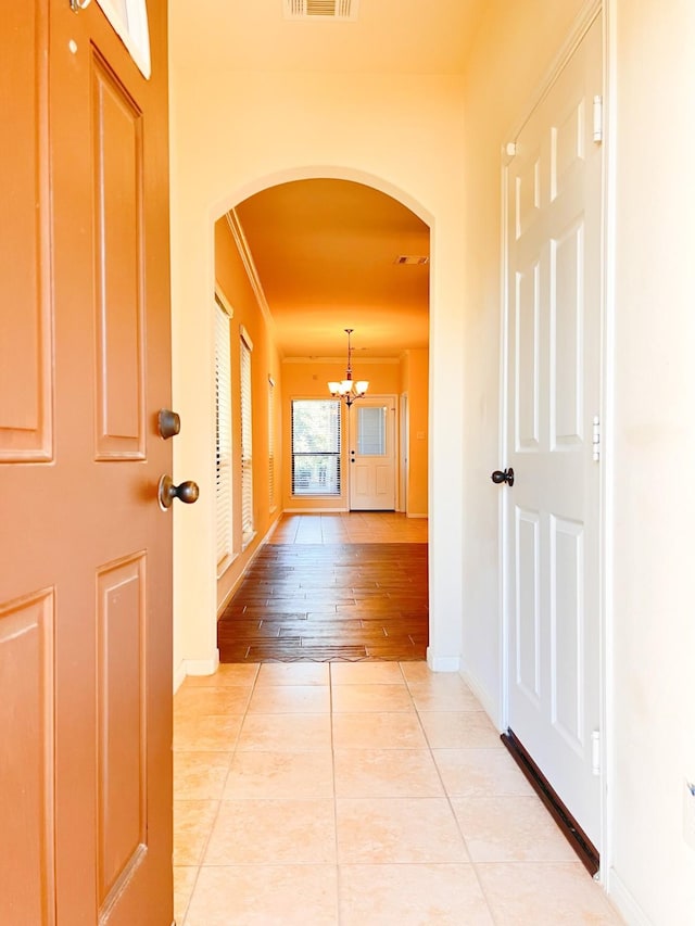 hallway featuring crown molding, a notable chandelier, and light tile patterned flooring