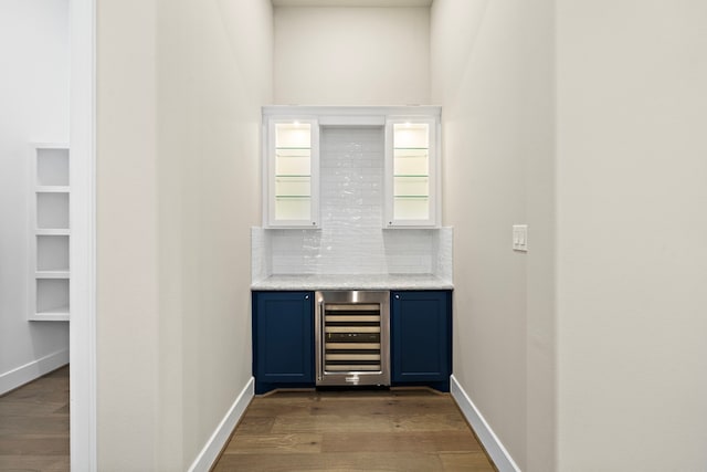 bar with tasteful backsplash, wine cooler, wood-type flooring, and blue cabinets