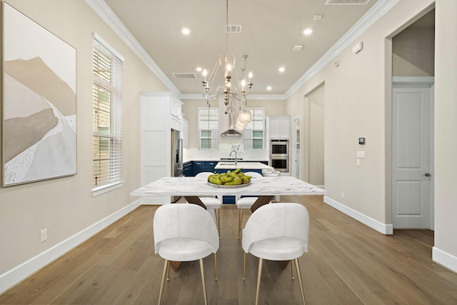 dining room featuring a notable chandelier, light hardwood / wood-style floors, crown molding, and sink