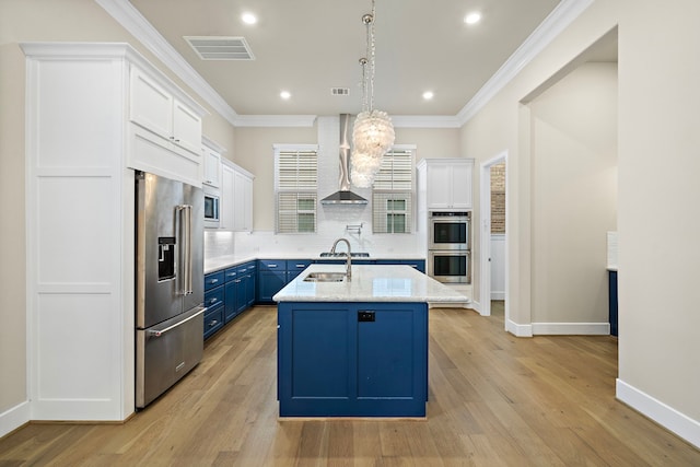 kitchen featuring white cabinets, wall chimney exhaust hood, blue cabinetry, appliances with stainless steel finishes, and tasteful backsplash