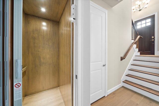 stairway with wood-type flooring, elevator, and an inviting chandelier