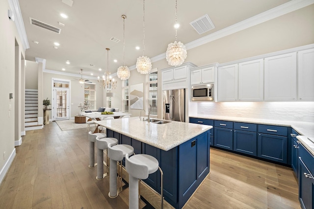 kitchen with appliances with stainless steel finishes, backsplash, ceiling fan with notable chandelier, a kitchen island with sink, and hanging light fixtures