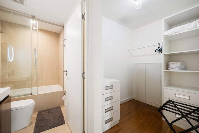 interior space featuring hardwood / wood-style floors, vanity, toilet, and bath / shower combo with glass door