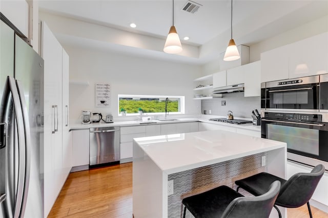 kitchen featuring stainless steel appliances, decorative light fixtures, a center island, light hardwood / wood-style floors, and white cabinetry