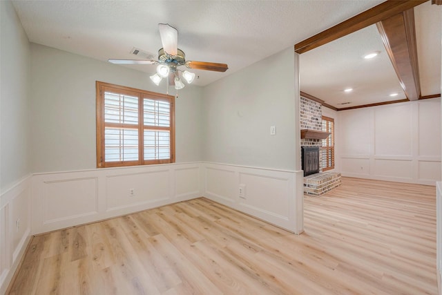 unfurnished living room with a textured ceiling, light wood-type flooring, a brick fireplace, and ceiling fan