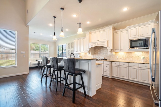 kitchen with stainless steel refrigerator, light stone countertops, hanging light fixtures, a kitchen bar, and a center island with sink