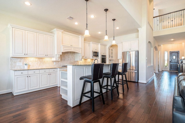 kitchen with light stone counters, stainless steel appliances, a kitchen island with sink, decorative light fixtures, and white cabinets