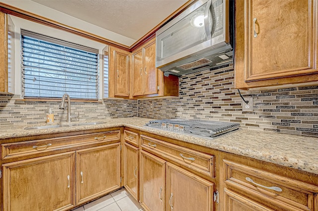 kitchen featuring light stone countertops, tasteful backsplash, sink, light tile patterned floors, and stainless steel gas stovetop