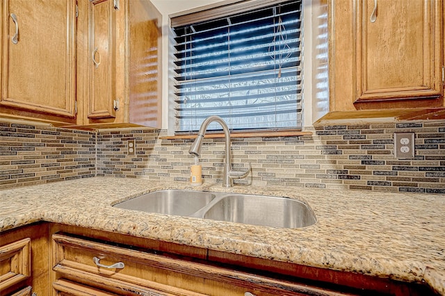 kitchen featuring backsplash, light stone countertops, and sink