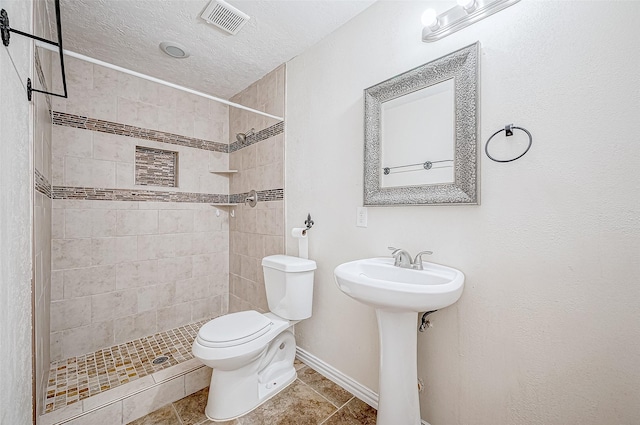 bathroom with tile patterned floors, sink, toilet, tiled shower, and a textured ceiling