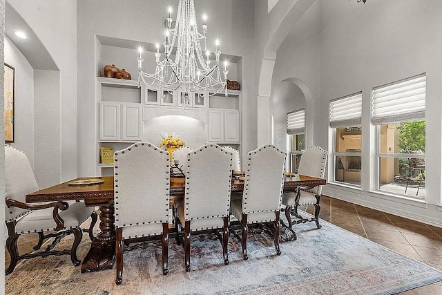 dining space with a towering ceiling, built in features, dark tile patterned floors, and a notable chandelier