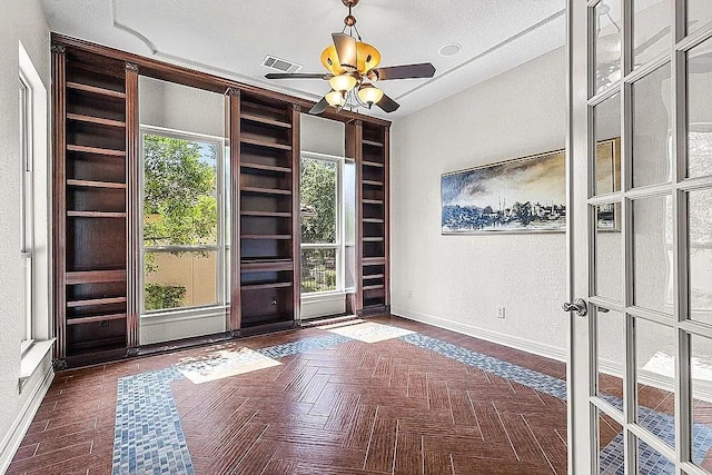 unfurnished room with ceiling fan, dark parquet flooring, a textured ceiling, and a wealth of natural light