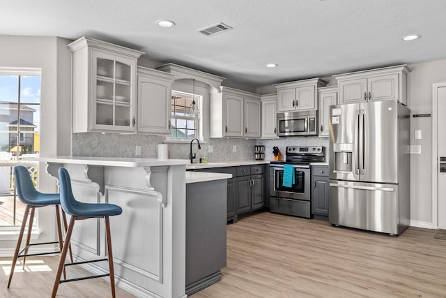 kitchen with gray cabinetry, a breakfast bar, light wood-type flooring, appliances with stainless steel finishes, and kitchen peninsula