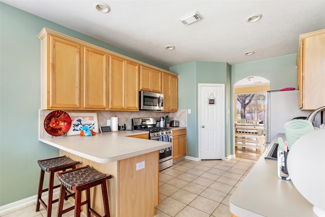 kitchen with stainless steel appliances, a kitchen breakfast bar, backsplash, kitchen peninsula, and light tile patterned floors