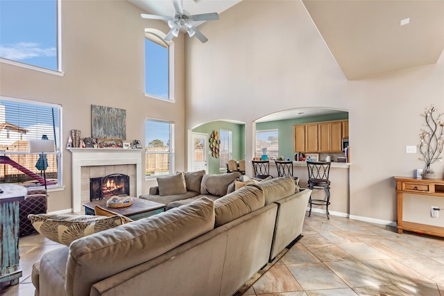 living room featuring a high ceiling, ceiling fan, and a tiled fireplace