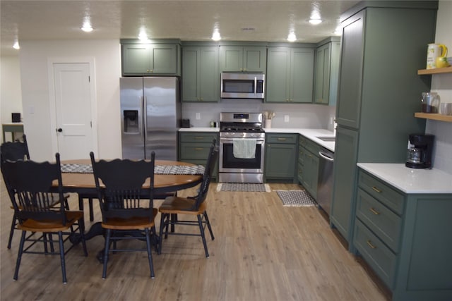 kitchen with tasteful backsplash, light wood-type flooring, appliances with stainless steel finishes, and green cabinetry