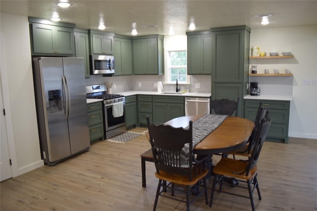 kitchen with green cabinets, sink, stainless steel appliances, and light hardwood / wood-style flooring