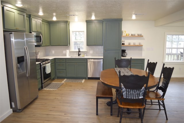 kitchen with sink, green cabinets, light hardwood / wood-style flooring, backsplash, and appliances with stainless steel finishes