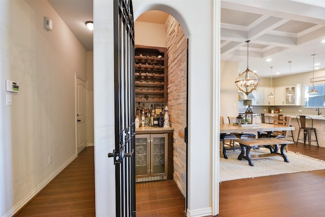 wine room with beamed ceiling, coffered ceiling, dark wood-type flooring, and an inviting chandelier