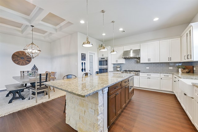 kitchen featuring coffered ceiling, a breakfast bar area, white cabinetry, a center island, and pendant lighting