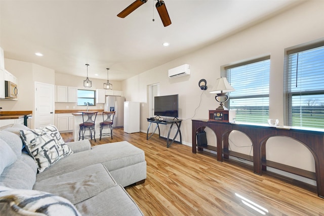 living room featuring ceiling fan, plenty of natural light, light hardwood / wood-style floors, and a wall mounted air conditioner