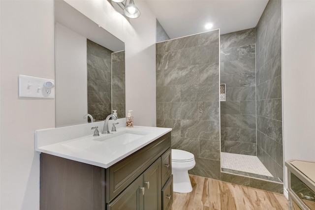 bathroom featuring hardwood / wood-style flooring, vanity, a tile shower, and toilet