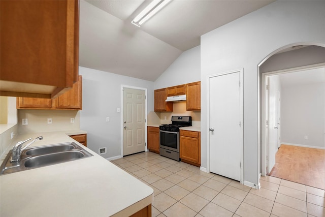 kitchen featuring stainless steel range with gas cooktop, sink, light tile patterned floors, and lofted ceiling