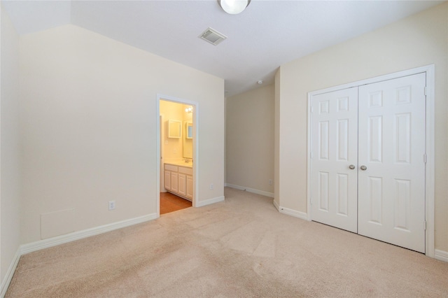 unfurnished bedroom with a closet, lofted ceiling, light carpet, and ensuite bath