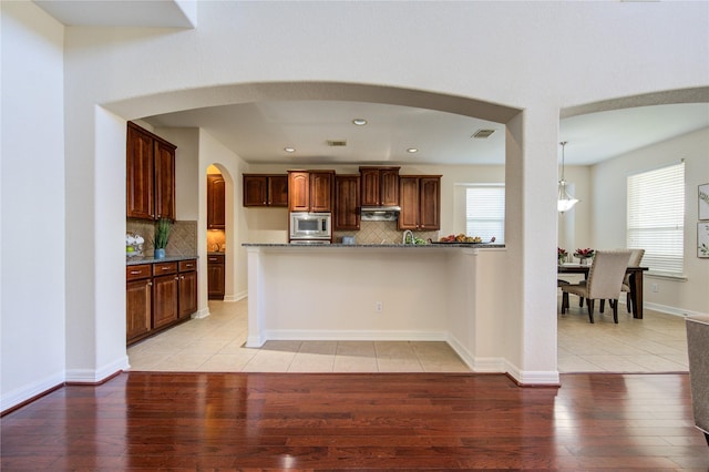 kitchen featuring tasteful backsplash, stainless steel microwave, dark stone countertops, light hardwood / wood-style floors, and hanging light fixtures