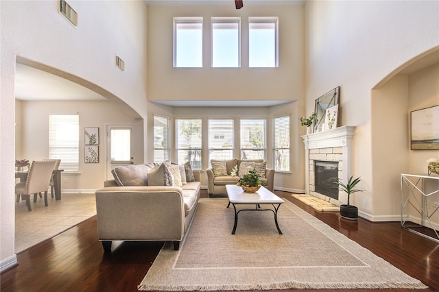 living room featuring a stone fireplace, hardwood / wood-style floors, and a towering ceiling