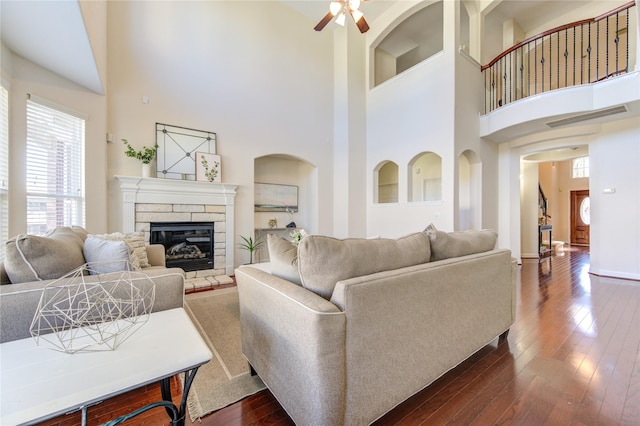 living room with a fireplace, a towering ceiling, dark hardwood / wood-style floors, and ceiling fan