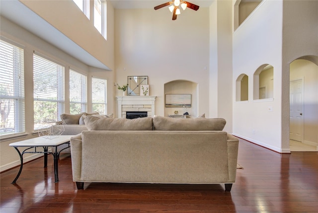 living room featuring a high ceiling, dark hardwood / wood-style floors, a stone fireplace, and ceiling fan