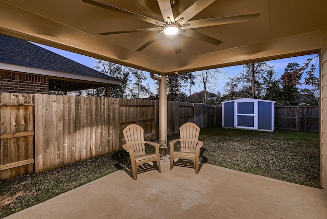 patio terrace at dusk with ceiling fan, a storage unit, and a lawn