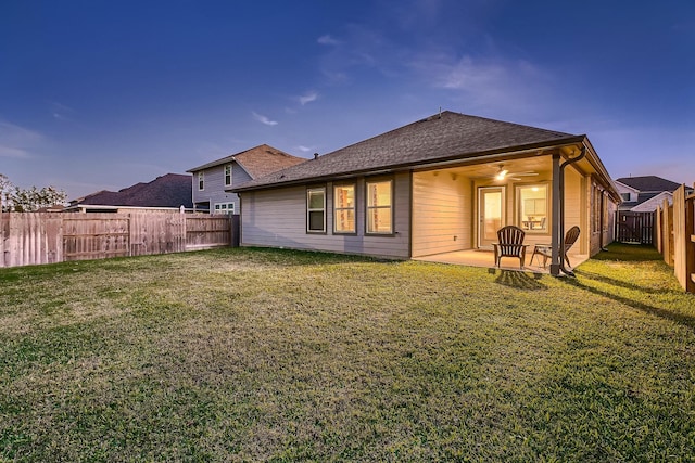 back house at dusk featuring a patio area and a lawn