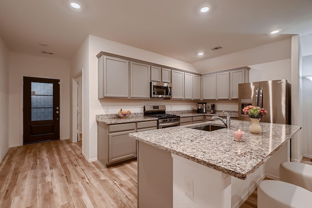 kitchen featuring gray cabinetry, a kitchen island with sink, sink, light stone countertops, and stainless steel appliances