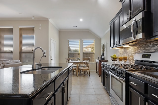 kitchen featuring lofted ceiling, dark stone counters, sink, an island with sink, and stainless steel appliances