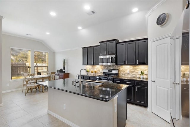 kitchen featuring a kitchen island with sink, dark stone counters, sink, vaulted ceiling, and stainless steel appliances