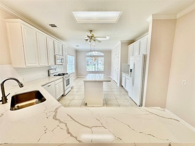 kitchen with white appliances, visible vents, white cabinets, a center island, and a sink