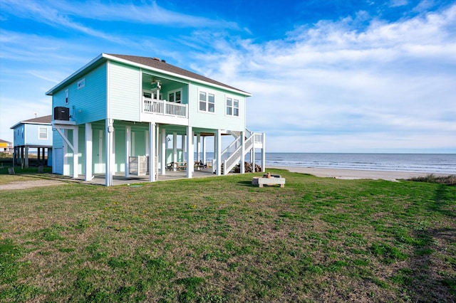 rear view of property featuring ceiling fan, a water view, a beach view, a patio, and a lawn