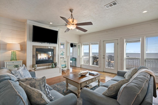 living room featuring a fireplace, ceiling fan, light hardwood / wood-style flooring, and a textured ceiling