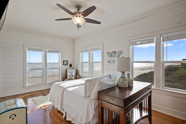 bedroom featuring ceiling fan, wood walls, dark hardwood / wood-style flooring, and a water view