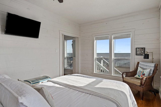 bedroom with ceiling fan, a water view, and wood walls