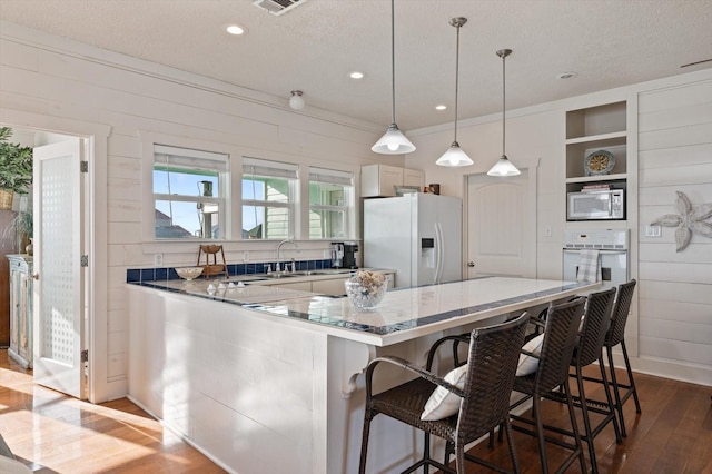 kitchen with wood-type flooring, a textured ceiling, decorative light fixtures, white appliances, and a breakfast bar