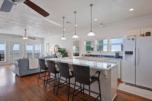 kitchen featuring pendant lighting, white appliances, ceiling fan, a textured ceiling, and a kitchen bar